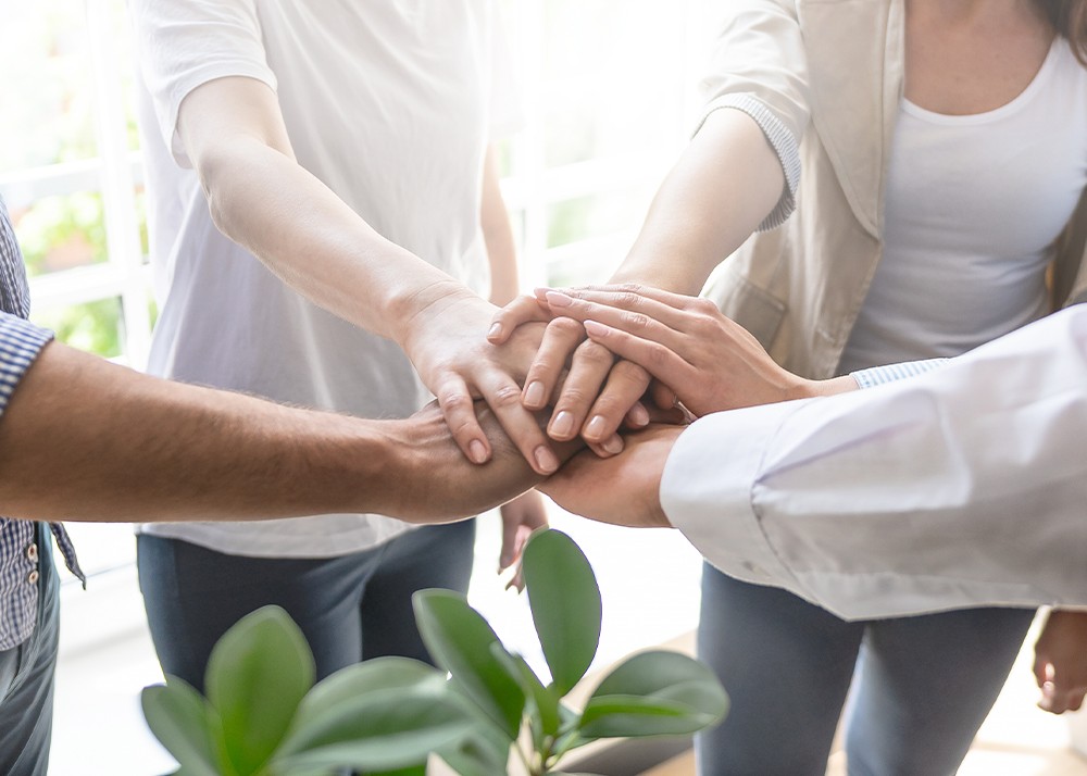 edoc blog vier Mitarbeitende legen die Hände zusammen für Teamwork, Zusammenhalt und optimale Zusammenarbeit