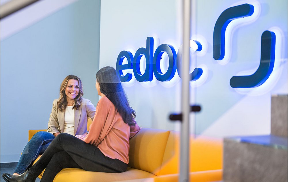 Zwei edoc Mitarbeiterinnen sitzen auf einem gelben Sofa und unterhalten sich über digitale ECM-Lösungen für ERP-Systeme