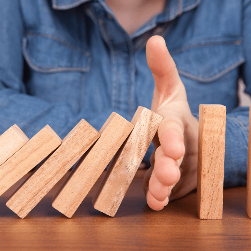 Reihe von Dominosteinen, bei denen eine Hand die Kette blockiert - eine einzige ausstehende Freigabe verzögert den gesamten Prozess