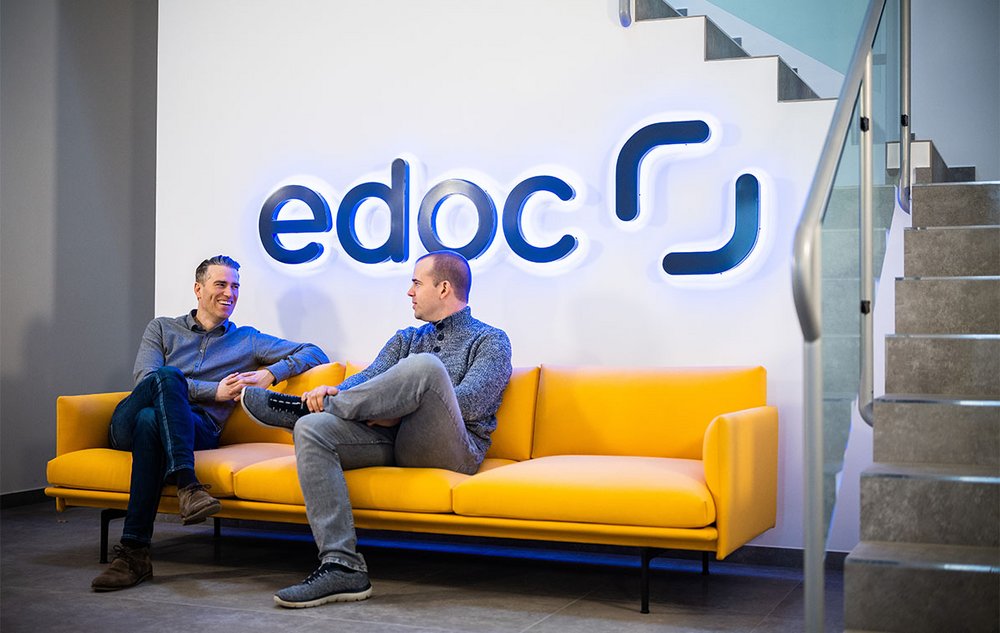 Zwei edoc Mitarbeiter sitzen auf einem gelben Sofa und unterhalten sich über digitale P2P-Prozesse
