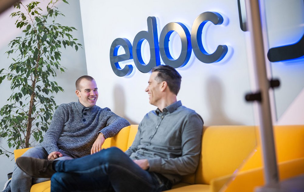 Zwei ECM-Spezialisten von edoc sitzen auf einem gelben Sofa und unterhalten sich